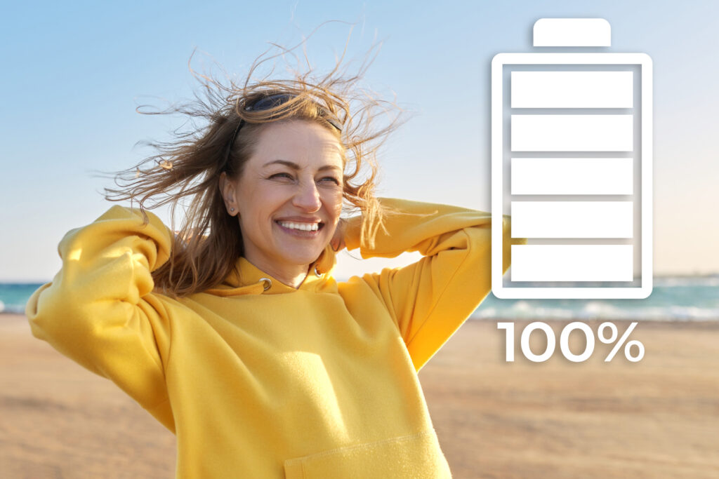Woman looking very happy on the beach with an illustration of a 100% charged battery